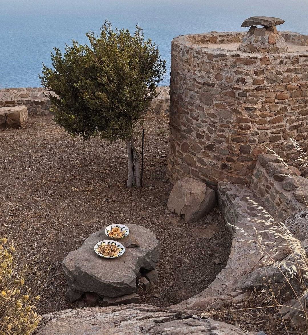 Παραδοσιακό κέρασμα σε πέτρινη αυλή με θέα, που συνδέει το προϊόν με τον τόπο και την εμπειρία επίσκεψης.
