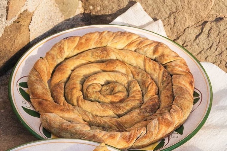 Μεγάλη σπειροειδής χειροποίητη πίτα σε παραδοσιακό πιάτο, έτοιμη για σερβίρισμα.