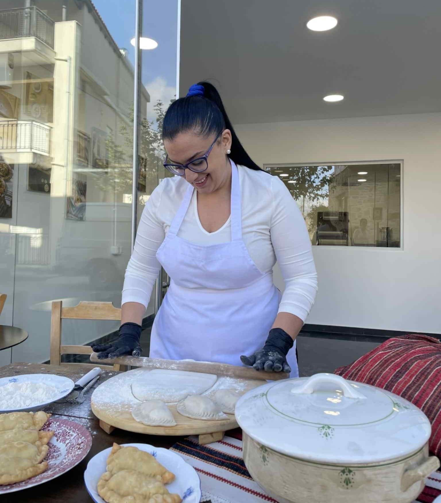 Σκηνή παραδοσιακής παρασκευής πίτας στον πάγκο εργασίας με σκεύη, ταψιά και χειροποίητη προετοιμασία.