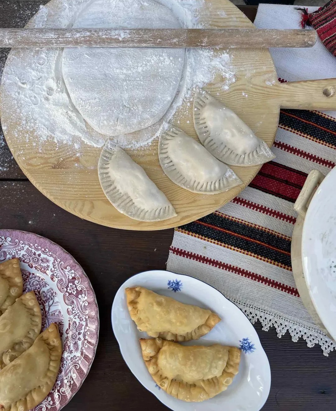 Παραδοσιακές πίτες και ανοιγμένο ζυμάρι σε υφαντό τραπεζομάντηλο, με έμφαση στη χειροποίητη παρασκευή.